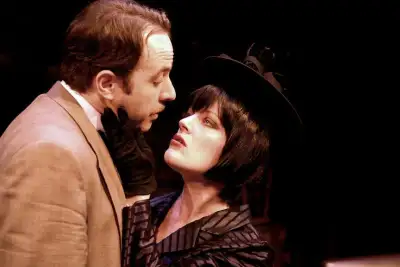 A woman with black hair is wearing a hat looking at a man standing next to her.
A woman dressed as a vampire looks up at a man beside her.