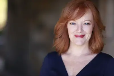 The woman has red hair and a blue shirt. She is smiling at the camera.