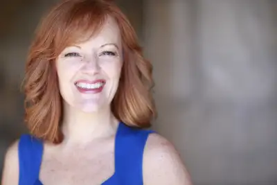 a woman with red hair wearing a blue top smiles brightly.