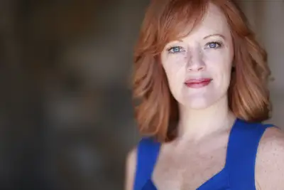 A woman with red hair poses for the camera. She is wearing a blue tank top.