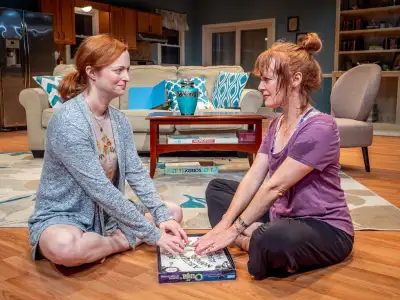 Two women sitting on the floor playing a game with a board that has letters on it.