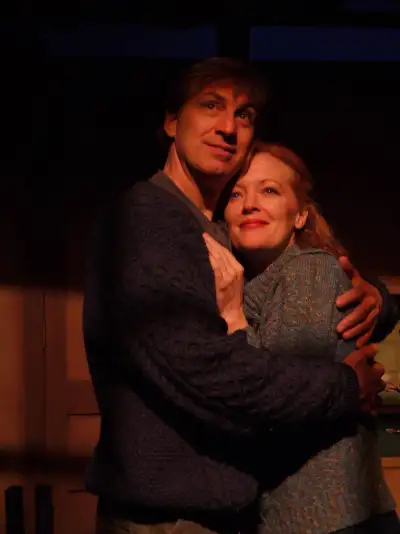 A man and woman are hugging in a dimly lit room with the man having his arm around the woman's waist.