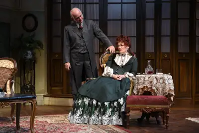 Man standing up while fixing the woman hair sitting on chair.
A man with glasses adjusting a woman's collar on a red dress.